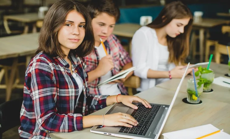 College students working on laptops and taking notes at a shared table