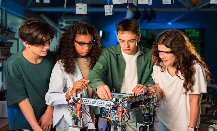 High school students in safety glasses wiring a robotics build together