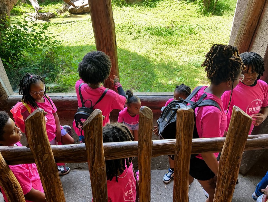 Campers looking out over a zoo exhibit through a wooden railing