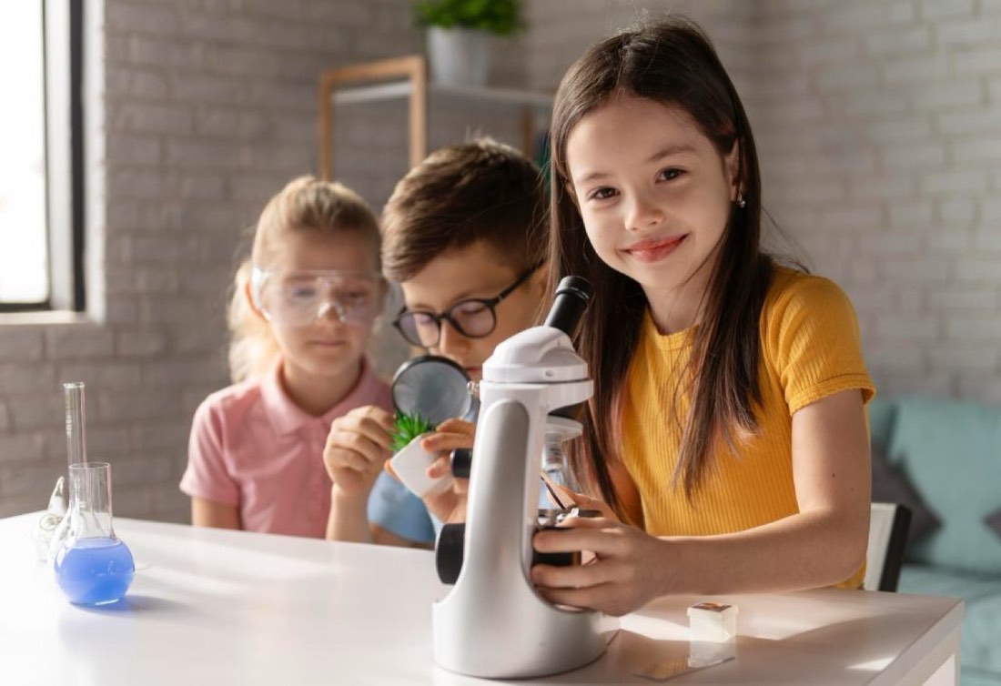 Three campers examining test tubes and a microscope during a STEAM activity