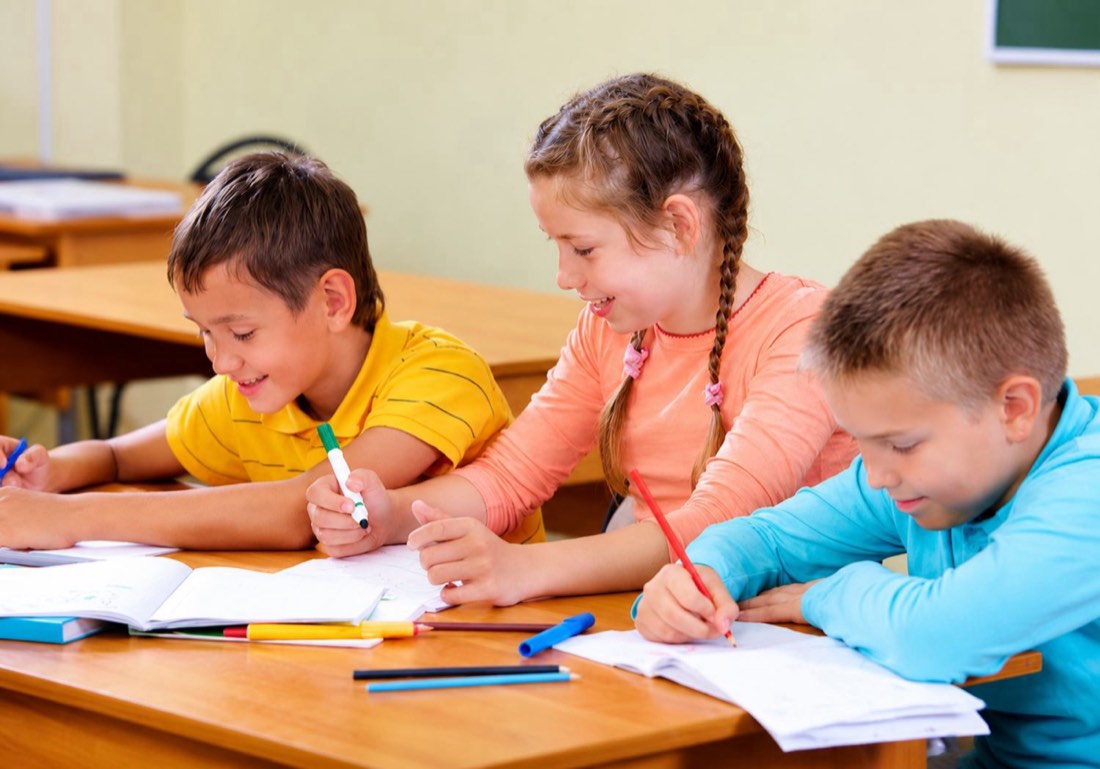 Three students writing together at a classroom desk